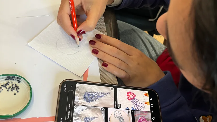 Person drawing jellyfish on paper, using phone reference.