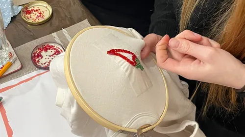 Person stickt rote Chili auf Stoff.