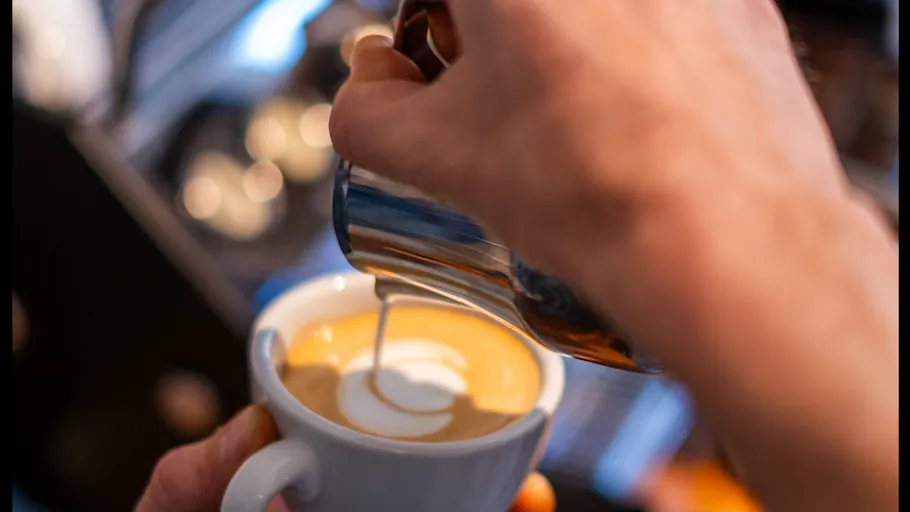 Hand pouring milk into coffee cup.