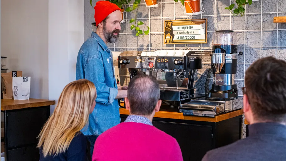 Barista demonstrating espresso machine to seated group.