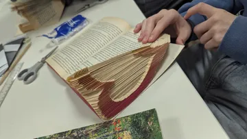 Hands folding book pages into heart shape.