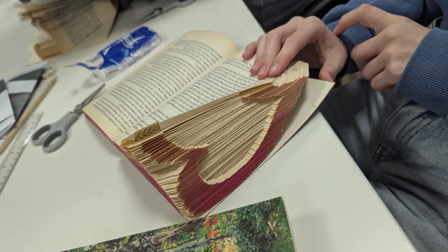 Hände falten Buchseiten zu Herzform.