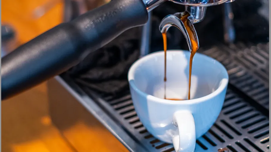 Espresso fließt in weiße Tasse auf Maschine.