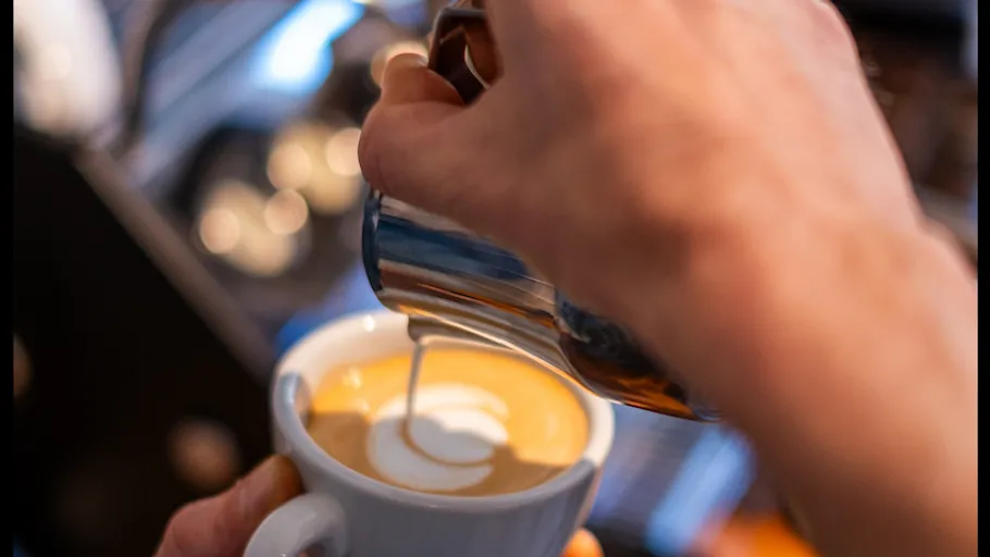 Hands pouring milk into coffee cup.