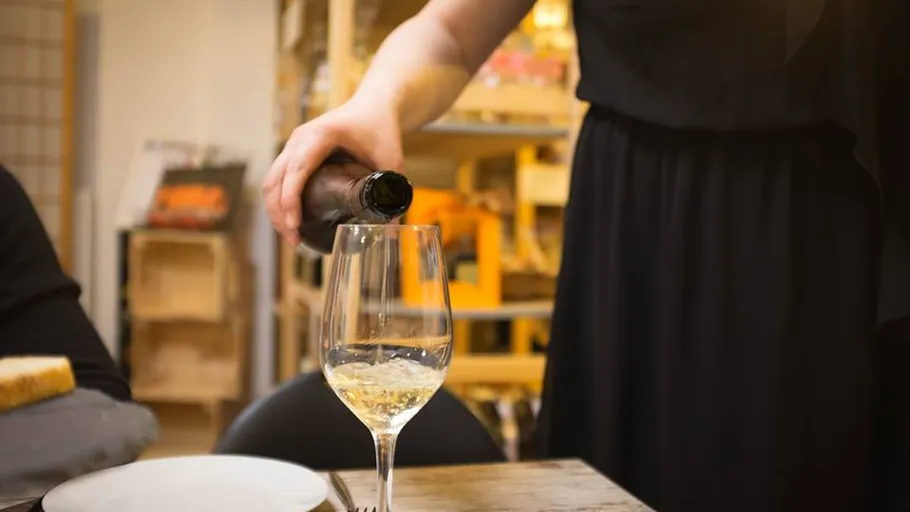 Person pouring wine into glass at table.