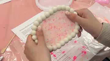 Hands holding a round object during crafting.