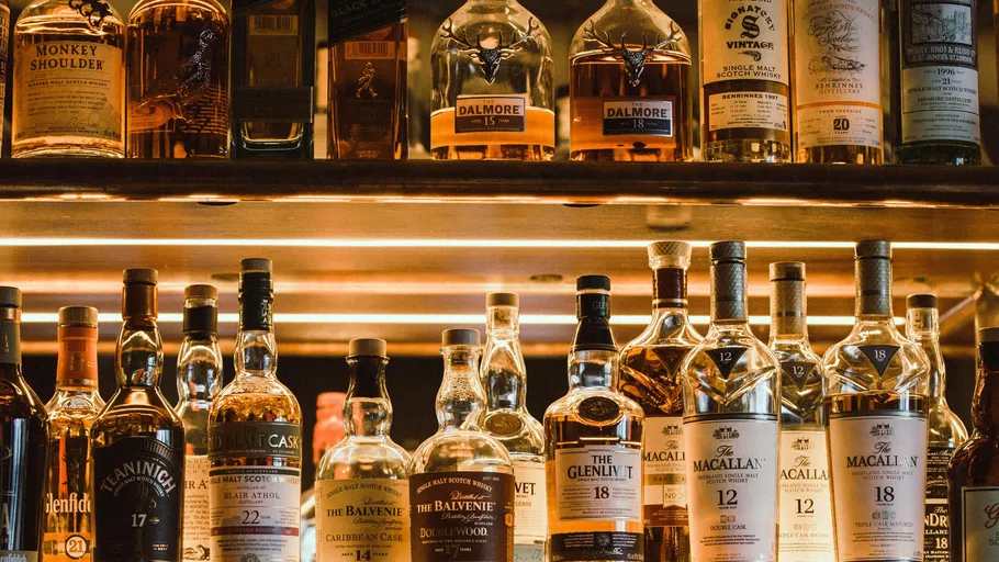 Various whiskey bottles on a wooden shelf.