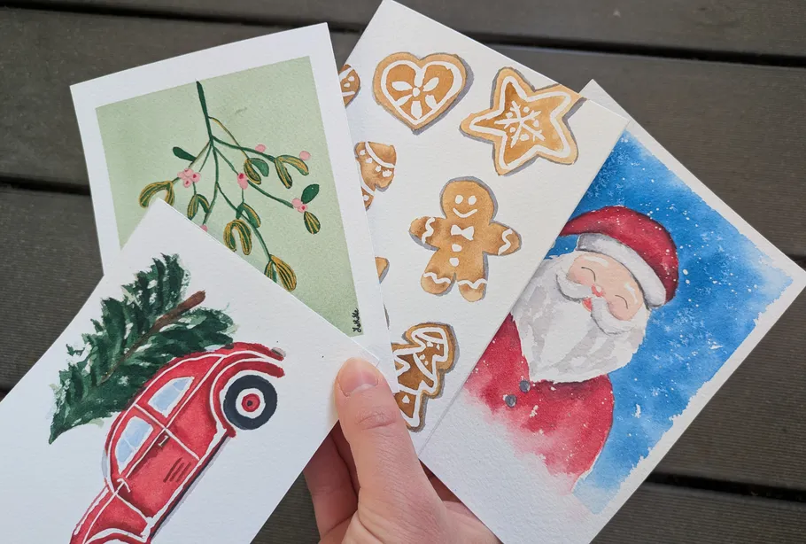 Hand holding four holiday-themed watercolor cards.