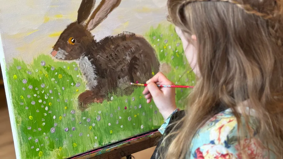 Girl painting rabbit in grassy field.