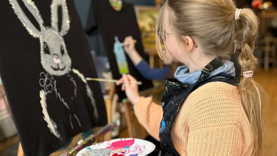 Person painting rabbit on black canvas.