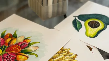 Bilder von Blumen, Avocado und Pommes auf Tisch.