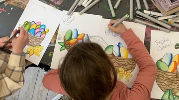 Kinder malen Ostereierkorb-Zeichnungen mit Filzstiften.