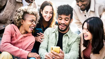 Friends laughing, looking at smartphone outdoors.