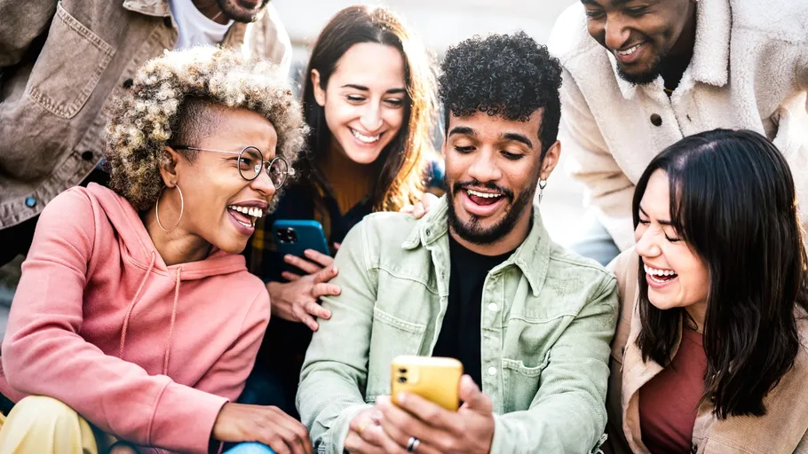 Freunde lachen, schauen draußen auf ein Smartphone.