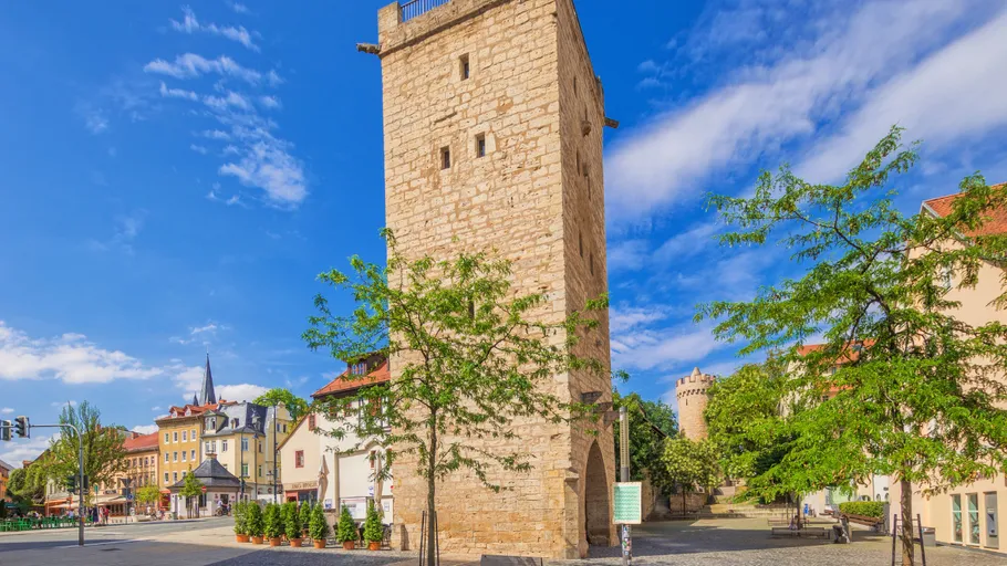 Steinturm auf Stadtplatz, von Bäumen umgeben.