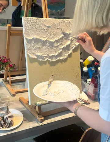 Person applies texture paste to canvas in studio.