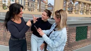 Three women laughing, pointing outside on bridge.