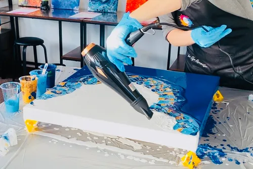 Person using hairdryer for paint pouring art.