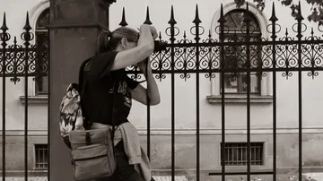 Person peers through ornate iron fence.