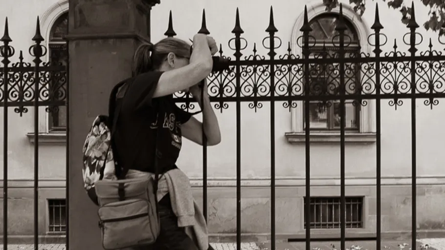 Person peers through ornate iron fence.
