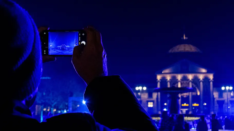 Person photographing illuminated building at night.