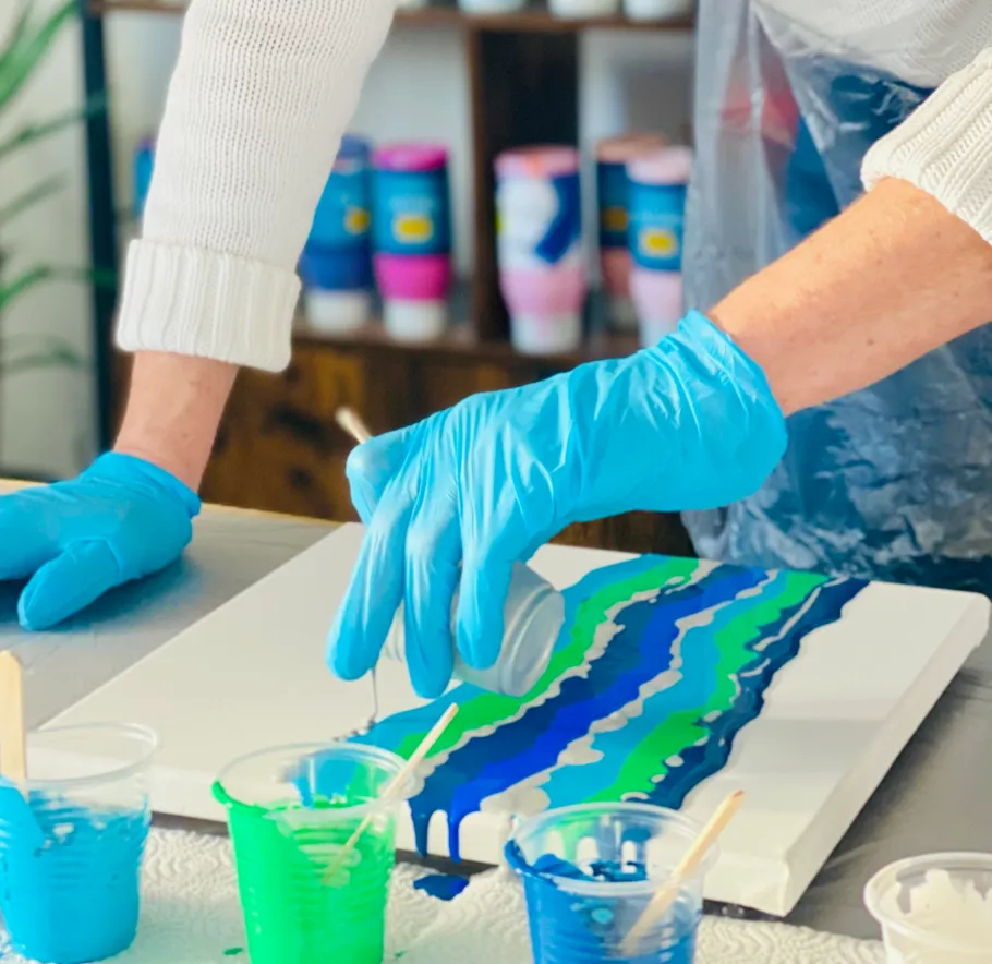 Person pouring paint on canvas, wearing gloves.