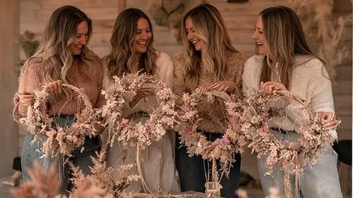 Vier Frauen halten Blumenkränze, lächeln drinnen.