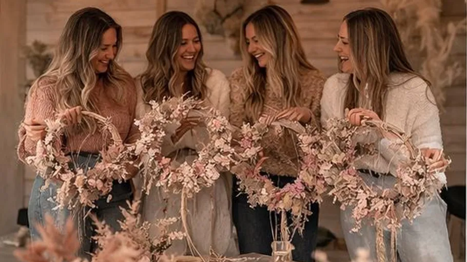 Vier Frauen halten Blumenkränze, lächeln drinnen.