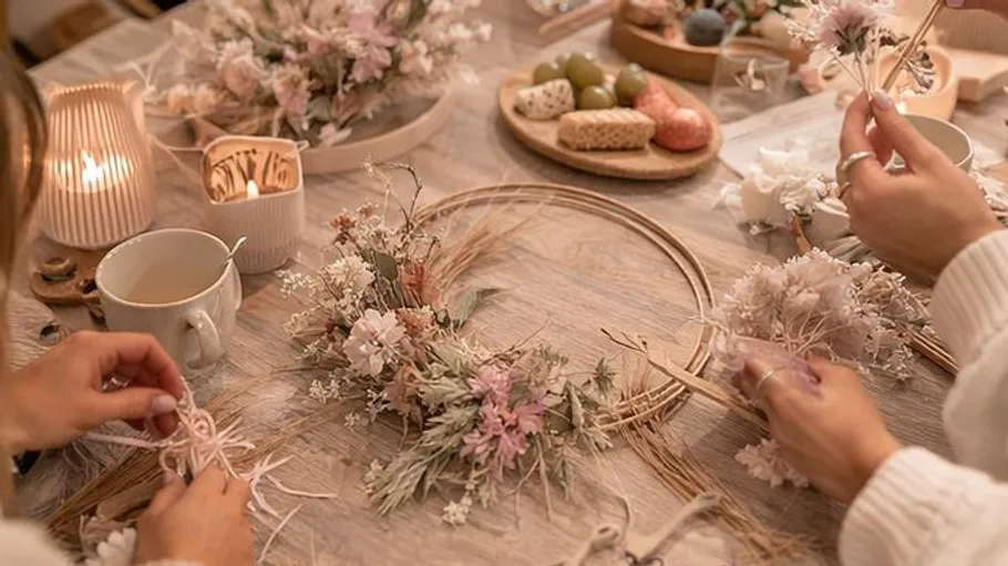 Hände basteln Blumenkranz auf Tisch.