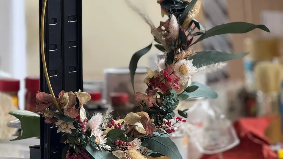 Dried floral wreath on black metal stand.