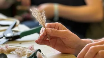 Hand crafting with dried plants on table.