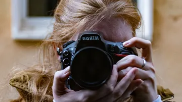 Person holding Nikon camera taking photo outdoors.