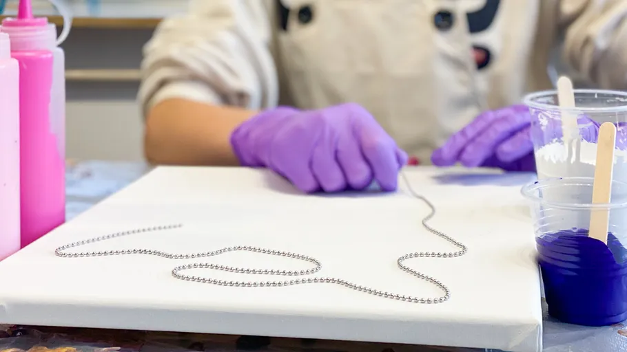 Person arranging chain on canvas for painting.