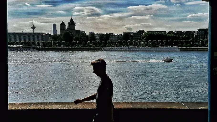 Silhouette of man walking by riverside cityscape.
