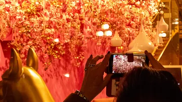 Person fotografiert pinke Blumeninstallation innen.