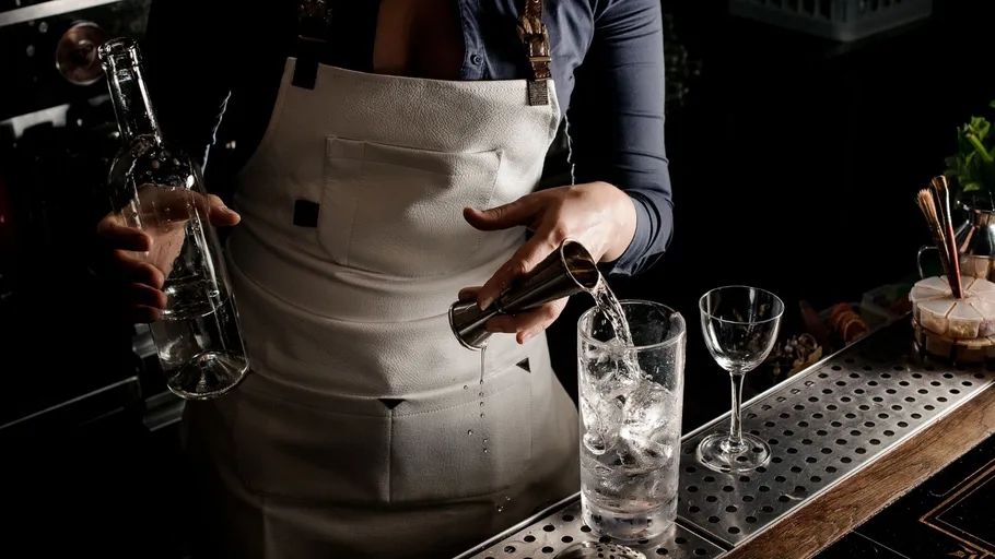 Bartender pouring drink into ice-filled glass.