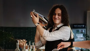 Bartender smiling while shaking a cocktail shaker.