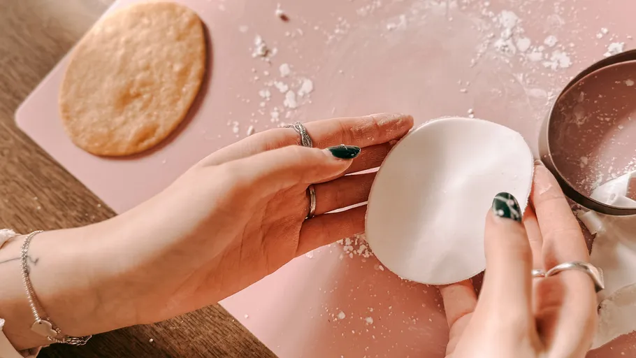 Hands shaping fondant on pink surface.