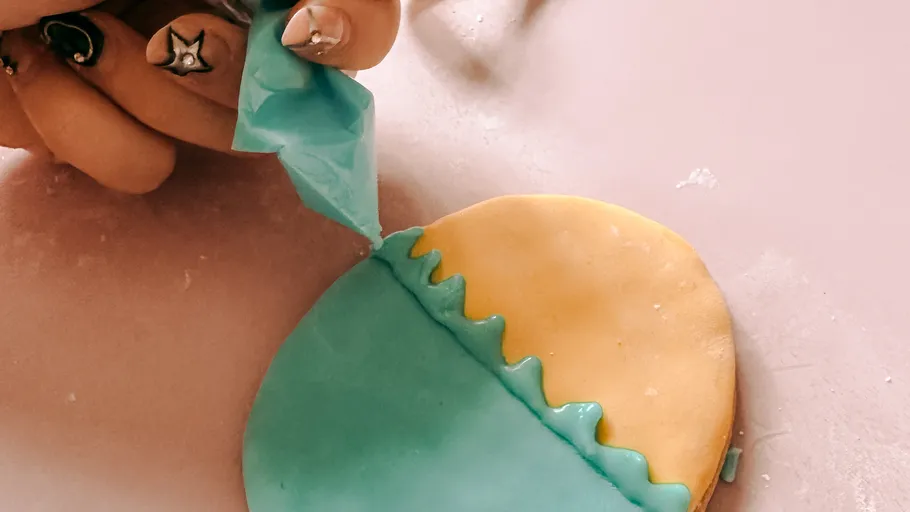 Hand decorates cookie with blue icing.