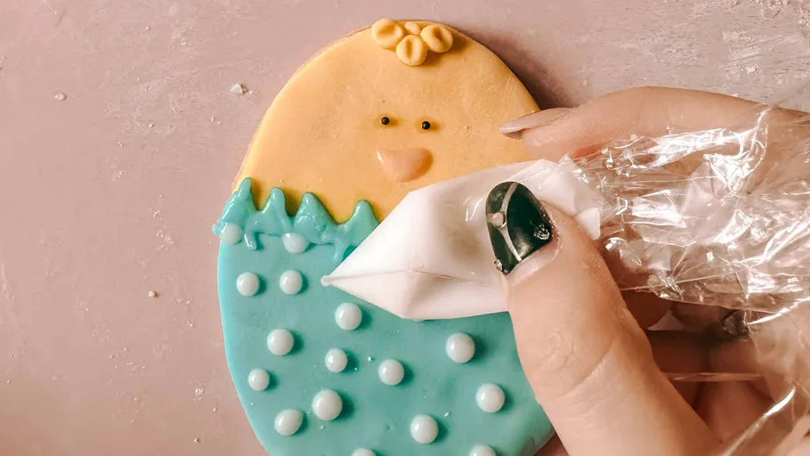Hand decorating cookie shaped like chick.