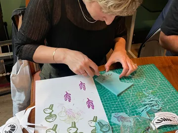 Person carving design at table with paper and tools.