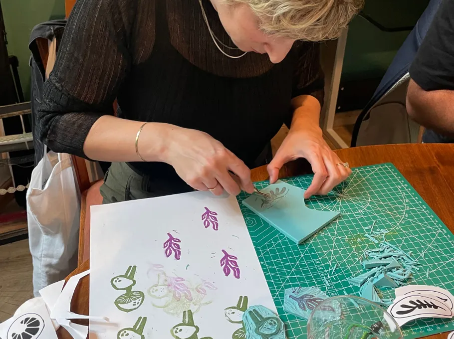 Person carving design at table with paper and tools.