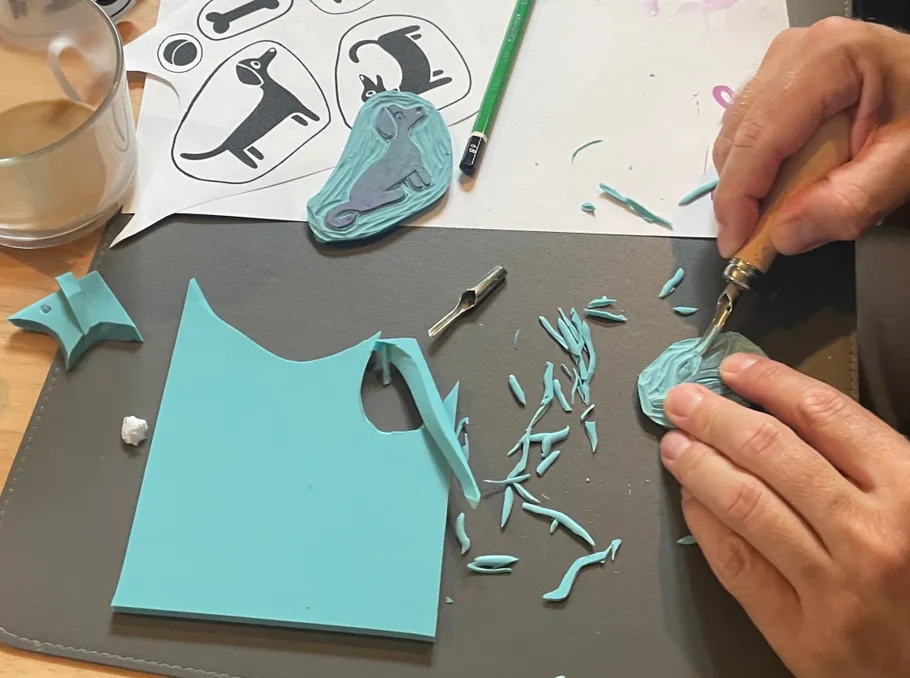 Person carving blue stamp on desk.