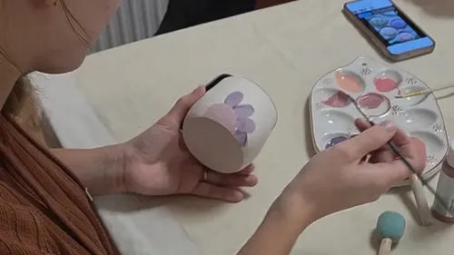 Person painting floral design on a mug.
