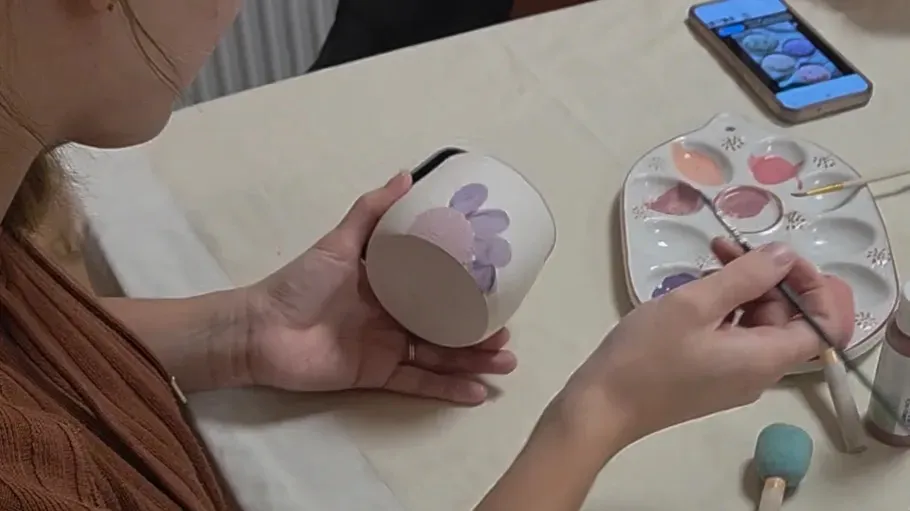 Person painting floral design on a mug.