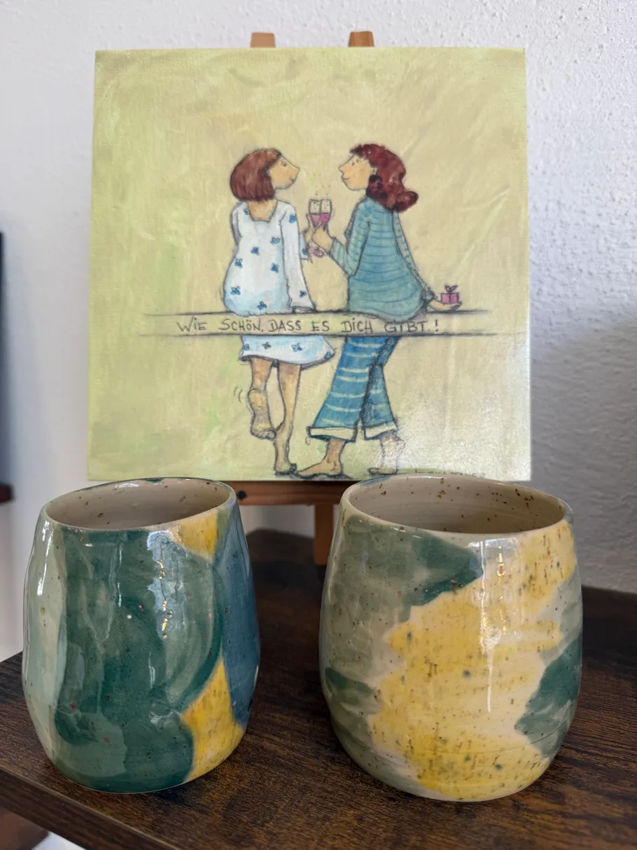 Two colorful cups in front of painting.