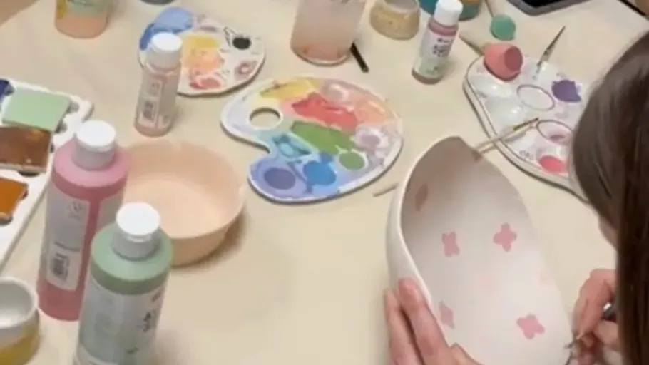 Person painting ceramic bowl at table.