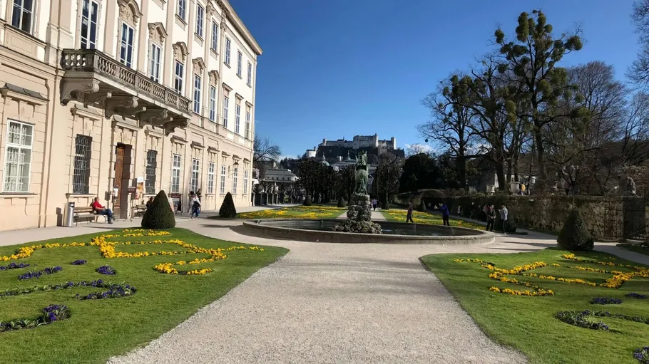 Garten mit Blumen, Statuen und historischem Gebäude.