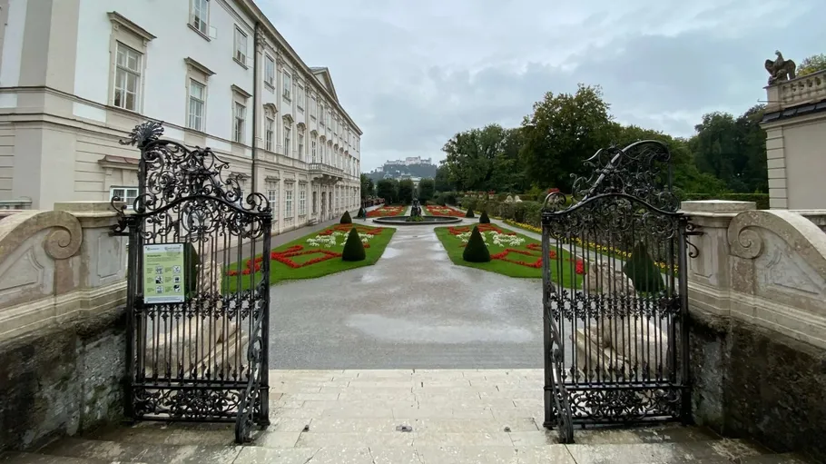 Ornate gates open to colorful garden, overcast sky.