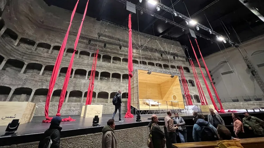Menschen auf Bühne mit roten Vorhängen, Steinwand.